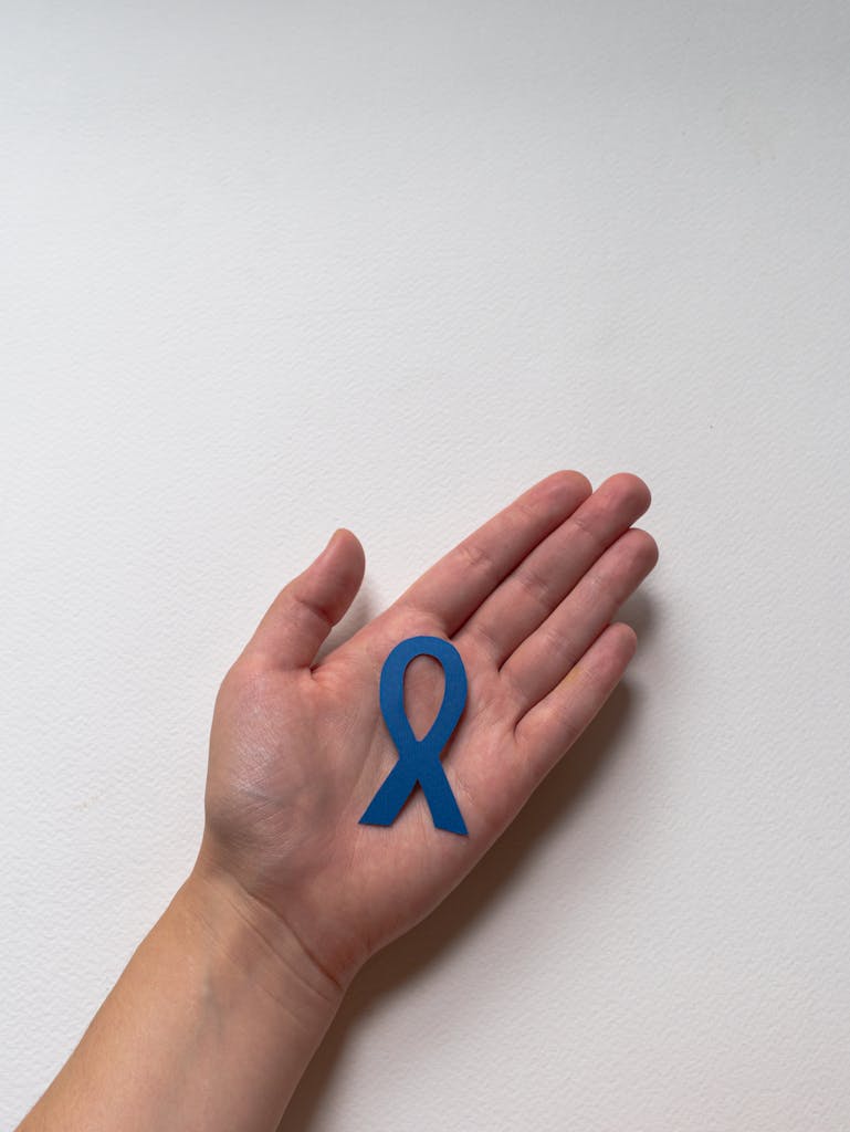 Close-up image of a blue awareness ribbon placed on a person's palm, symbolizing support and awareness.